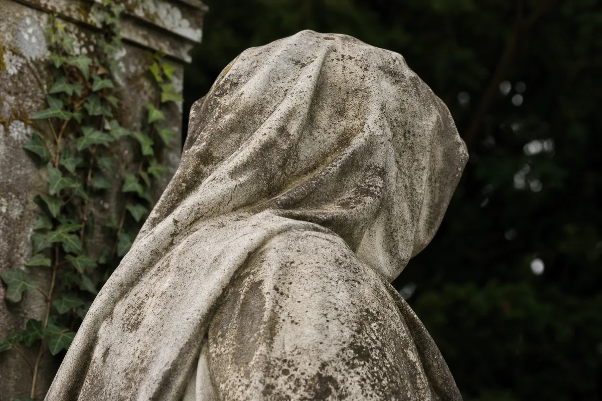 Sculpture funéraire en pierre patinée dans une allée boisée du Père-Lachaise