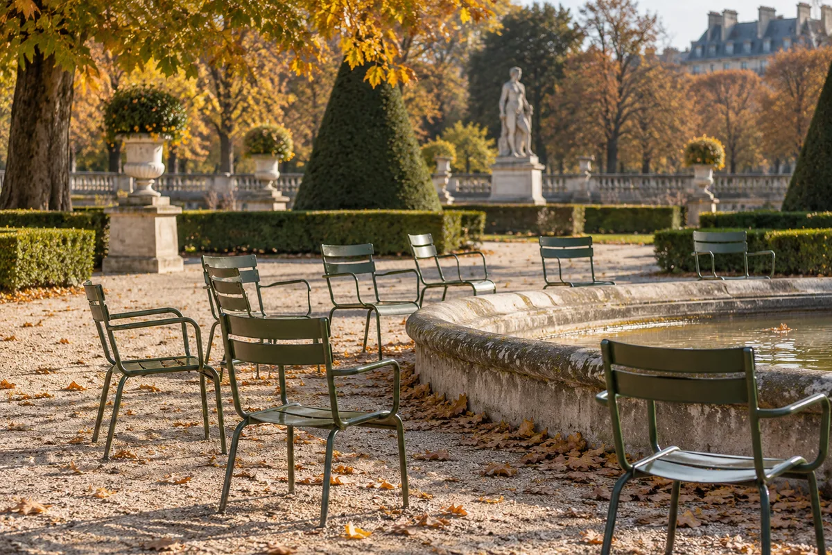 Allée d’un jardin parisien bordée de chaises métalliques vertes vides sous une lumière d’automne